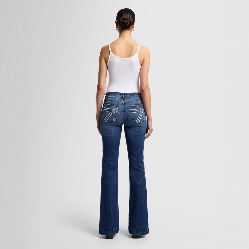 Woman wearing  DOJO Lake Blue flared jeans and a white tank top on a light gray background
