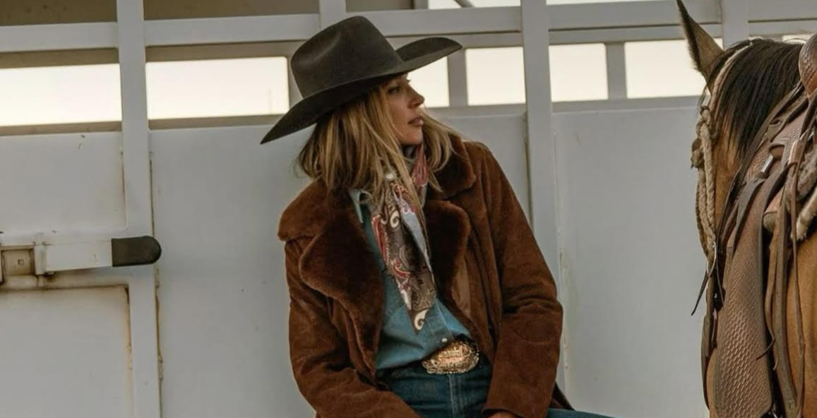 Person in cowboy attire sitting on a truck bed next to a horse